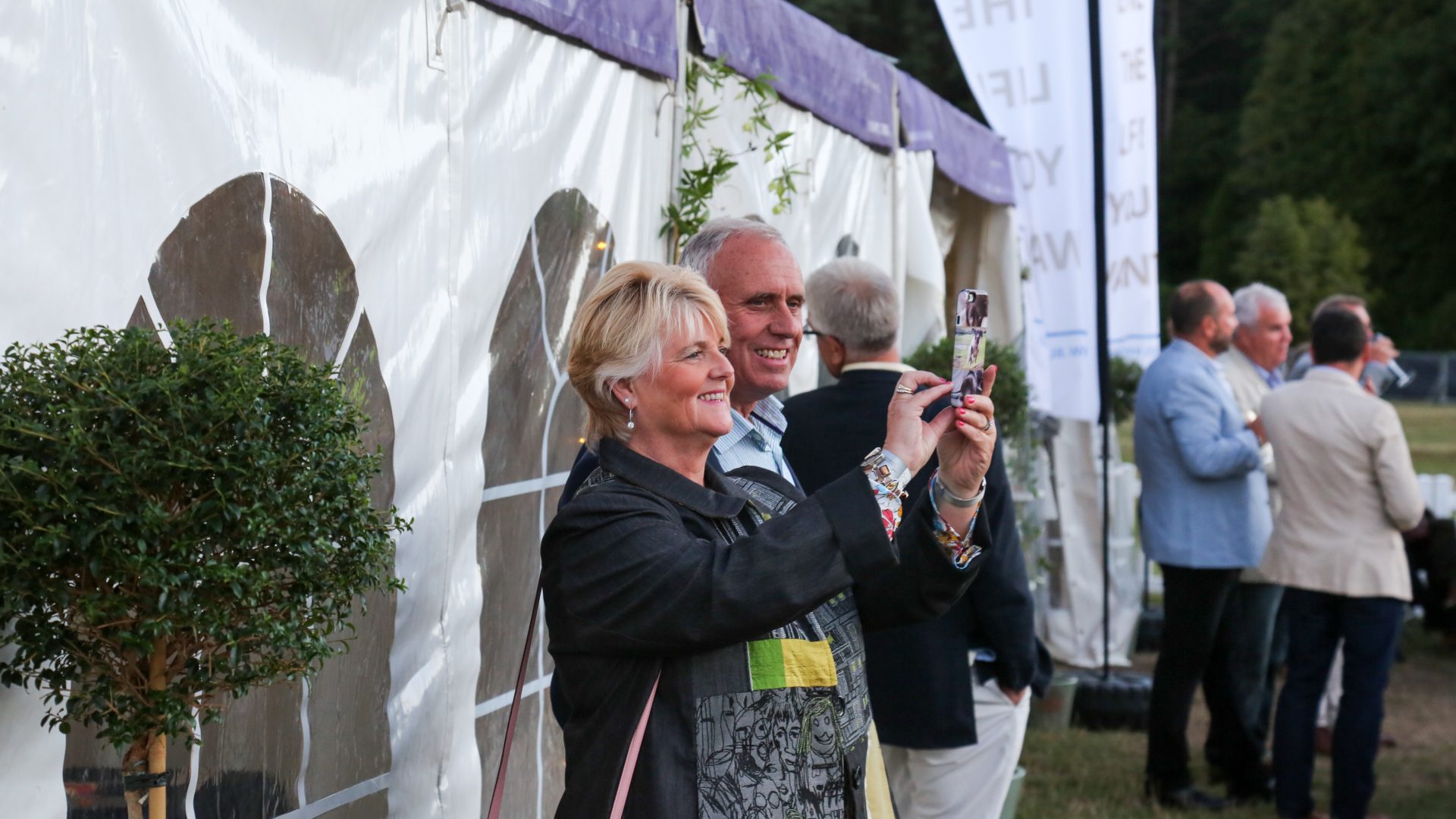 Two guests take a photo in front of the Corporate Guests marquee at the BSO Proms in the Park, which aims to enterain and impress other guests.