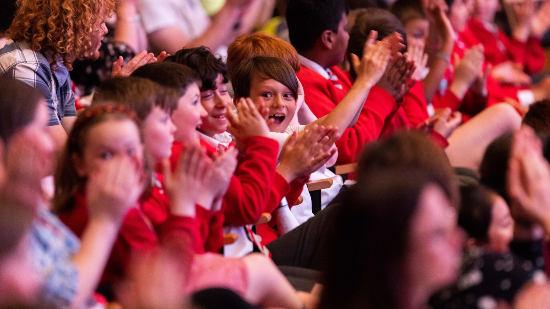 Shows children having fun at an orchestral concert. They are clapping hands and smiling.